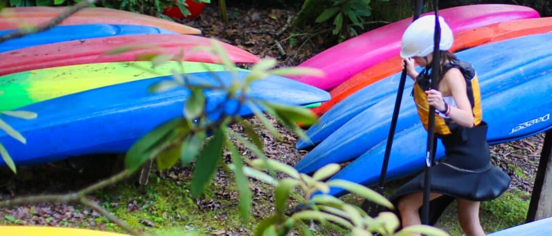 camp girl and row of whitewater kayaks